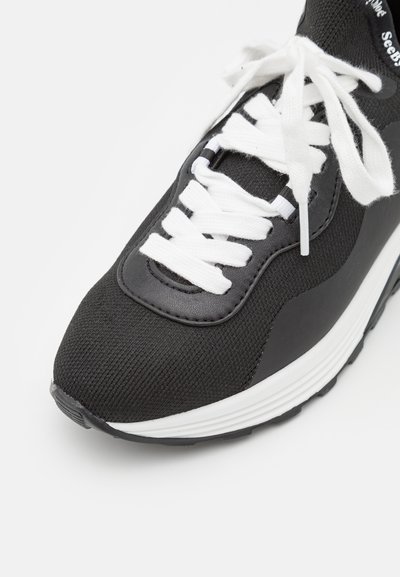 Zwarte sneaker met een gestructureerde stoffen bovenkant, leren accenten, witte veters en een witte tussenzool. Beschikt over een laag profiel en rubberen buitenzool.