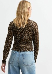 Haut à manches longues à imprimé léopard marron et noir avec un ourlet festonné, associé à un jean en denim taille haute bleu clair.