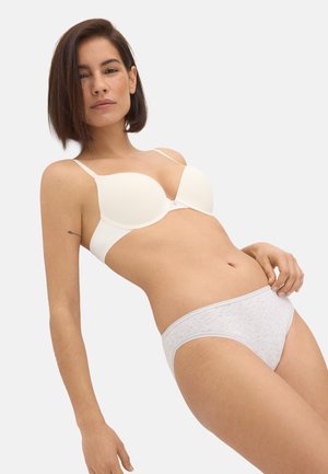 Mujer con un sujetador blanco acolchado y bragas de color gris claro con estampado, posando sobre un fondo blanco liso.