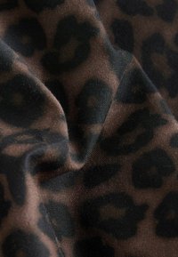 Tissu doux avec un motif léopard brun et noir, présenté en gros plan avec des plis et des détails de texture.