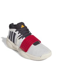 Idrottssko med ett överdel av vit mesh, röd rem med perforeringar, marinblå detaljer och en strukturerad gummisula. Har tre svarta ränder.