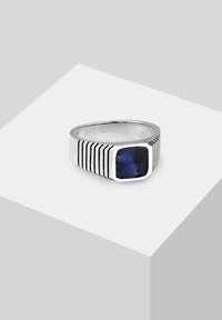 Sudraba gredzens ar kvadrātveida zilu akmeni, ar vertikālām svītru rotājumiem uz gredzena joslas un pulētu apdari.