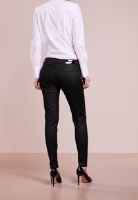 Svarta slim-fit byxor i stretchmaterial med en mjuk textur, bakfickor och diskreta sömdetaljer, tillsammans med en vit skjorta.