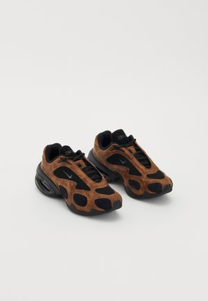 Brązowe zamszowe i czarne siateczkowe sneakersy o zaokrąglonym kształcie, z wyraźnymi wycięciami i masywną czarną podeszwą.