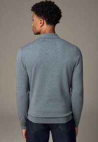 Helle blaue Strickpullover mit langen Ärmeln, einem kragenförmigen Ausschnitt und geripptem Saum. Hergestellt aus weichem Stoff mit einer glatten Textur.