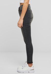 Crne skinny traperice visokog struka s raspucanim rubom, izrađene od trapera, uparene s bijelim tenisicama. Imaju uski kroj i standardne stražnje džepove.