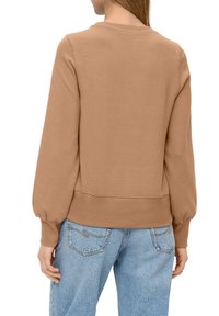 Bruine sweatshirt met lange pofmouwen en geribbelde halslijn en zoom. Gekoppeld aan lichtblauwe denim jeans, met een ontspannen pasvorm en stoftextuur.