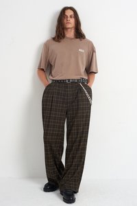 Brązowy, oversize t-shirt z logo "RAGGED", w połączeniu z szerokimi spodniami w kratkę w ciemnozielonym i brązowym kolorze, wyposażonymi w czarny pasek z srebrnym łańcuchem.