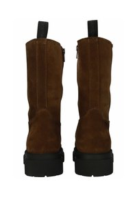 Pareja de botas de ante marrón con suelas gruesas negras, vista trasera que muestra costuras verticales y tiradores negros con texto.