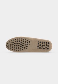 Beige Schuhsohle mit schwarzen Gummigriffen, die in Clustern an Fersen- und Zehenbereich auf einem einfarbigen hellen Hintergrund angeordnet sind.