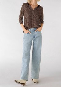 Blouse marron à motifs avec un col en V et des manches trois-quarts, associée à un jean large bleu clair et des bottines beiges.