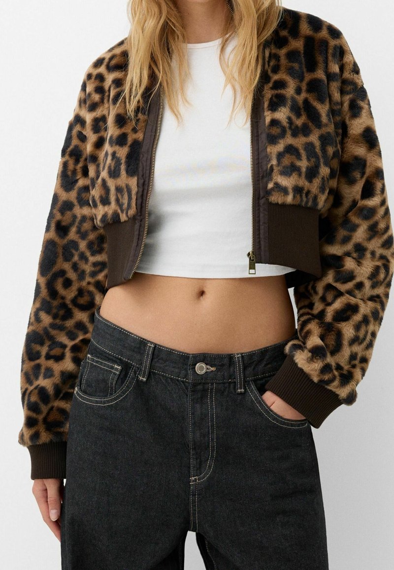 Giacca bomber tagliata in pelliccia sintetica leopardata con polsini e orlo a coste marroni, abbinata a jeans in denim scuro e una maglietta bianca.