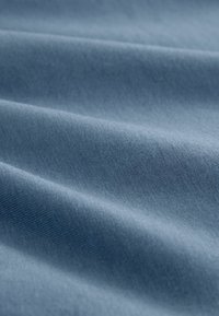 Kék szövet sima textúrával, finom redőkkel és egyenletes szövésmintával. A szín egy lágy, tompított kék árnyalat.