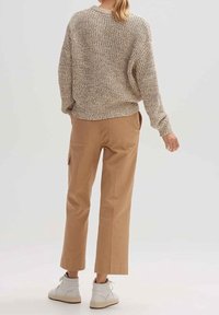 Gruba, beżowa sweter, w luźnym kroju, w połączeniu z beżowymi spodniami o szerokich nogawkach i białymi trampkami za kostkę. Neutrala paleta kolorów, teksturowana tkanina.