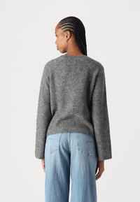 Pull en maille gris avec une coupe décontractée, texture côtelée, encolure arrondie et manches longues. Associé à un jean large bleu clair.