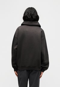 Εξαντλητικού μεγέθους, σκουρόχρωμο γκρι φούτερ από μαλακό υλικό. Υψηλός γιακάς με φαρδιά μανίκια, ριμπ μανσέτες και πάτο. Μινιμαλιστικός σχεδιασμός, χωρίς εμφανές λογότυπο.