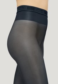 Collant neri semi-opachi con una texture liscia e una fascia in vita con il logo "Wolford". Prodotto mostrato su sfondo neutro.