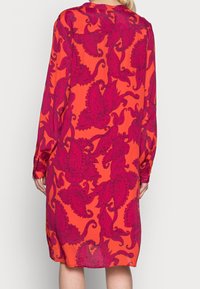 Abito a maniche lunghe in tessuto arancione brillante, con un grande motivo paisley rosa, dotato di polsini con bottoni e una vestibilità comoda.