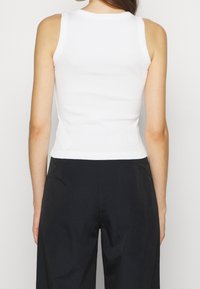 Vit bomullstopp med en figurnära design, rund halsringning och ribbad textur, bärs tillsammans med lösa svarta byxor. En enkel och mångsidig stil.