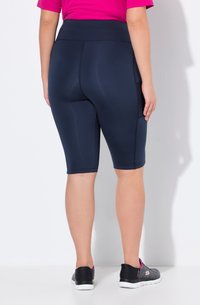 Meripimeä polkupyöräshortsit joustavasta kankaasta, korkea vyötärö, päättyy juuri polven ylle. Yhdistetty mustiin urheilukenkiin, joissa on vaaleanpunaisia yksityiskohtia.
