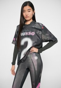 Overdimensjonert svart t-skjorte med grafisk trykk, som har "2" og "Paola Russo." Kombinert med tettsittende svart og rosa mønstrede leggings.