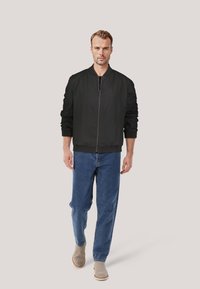 Schwarze Bomberjacke mit Reißverschluss, gerippten Bündchen und Saum, kombiniert mit hellblauen, gerade geschnittenen Jeans und beigen Knöchelstiefeln.