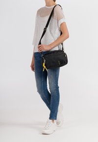 Černá nylonová crossbody taška s texturovaným povrchem, stříbrným kováním a žlutým táhlem zipu. Disponuje ramenním popruhem a detailem s logem.