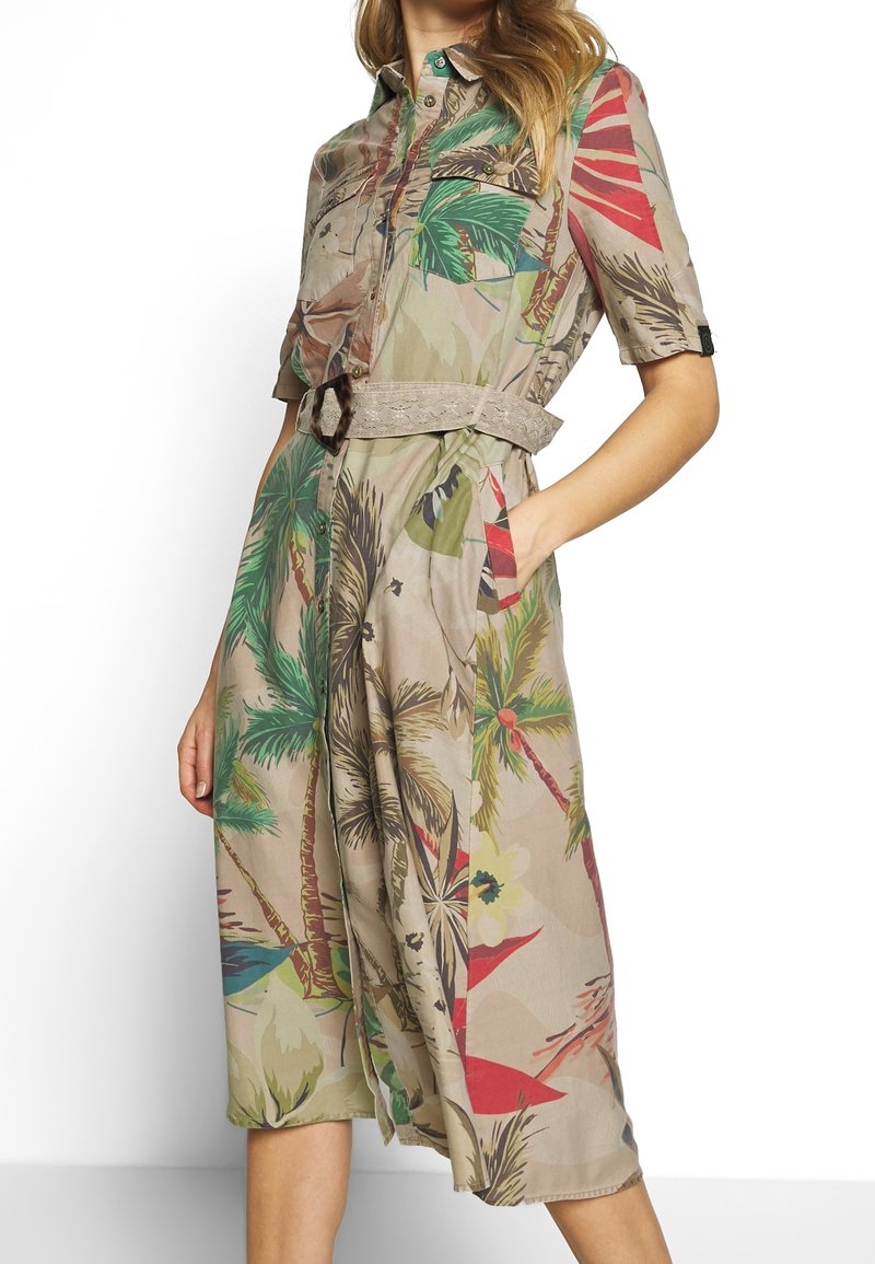 Abito camicia a maniche corte in tessuto beige chiaro con stampa di foglie e fiori tropicali, vita con cintura e tasche laterali.