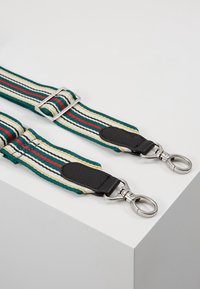 Pásek v zelených, krémových a červených pruzích, s černými koženými detaily a kovovými sponami. Obdélníkový tvar, celoplošná tkaná textura.