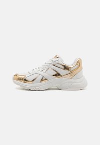 Valkoinen sneaker kultaisilla yksityiskohdilla, jossa on teksturoitu pinta, verkkomateriaalista valmistetut paneelit ja pehmustettu pohja. Naruja pidetään paikoillaan vahvistetuilla nauhakupeilla.