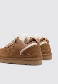 Zapatillas de ante marrón y malla con forro de piel sintética, detalladas con un acento blanco, ojales metálicos y suelas texturizadas.