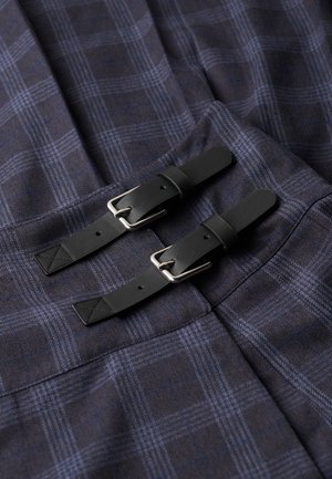 Marinekarierter Stoff mit hellblauen Linien, versehen mit zwei schwarzen Lederriemen mit silbernen Schnallen und kontrastierenden Steppnähten.