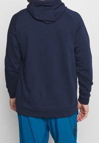 Marinblå hoodie med en texturerad yta, utrustad med en stor luva och långa ärmar. Den har en avslappnad passform och en ribbad nederkant.