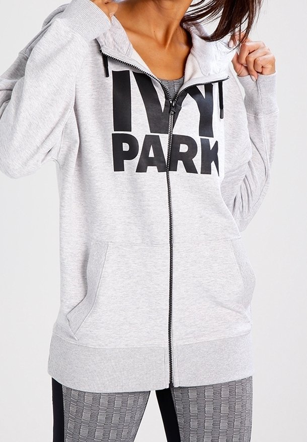 Szara bluza z kapturem na suwak, z dużym czarnym napisem "IVY PARK", z kapturem ze sznurkiem i przednimi kieszeniami, wykonana z miękkiego, teksturowanego materiału.