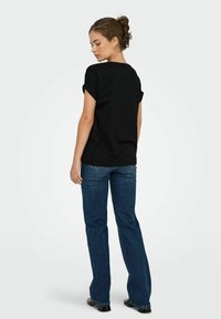 Sort kortærmet top med optrukne manchetter, parret med blå flare jeans. Glat stofstruktur, enkelt design og ingen synlige mønstre.