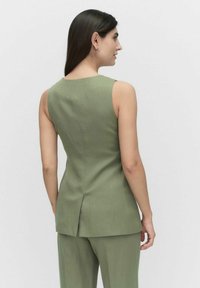 Grön ärmlös topp med en figursydd form, med en ventil bak och en smidig tygtextur. Stylad med matchande byxor.