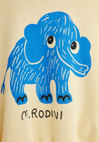 Kindlicher blauer Cartoon-Elefant mit weißen Linien und großen Augen, stehend über dem Text "m. RODINI" auf einem beigen Stoffhintergrund.