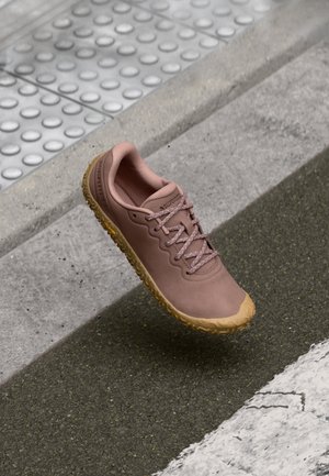 Light pink athletic shoe with a textured uppers, rubber sole, and round laces. Slightly curved toe and pronounced tread pattern on the sole.