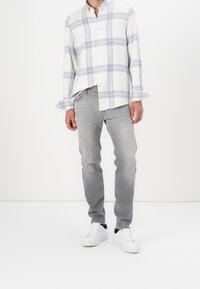 Geruit overhemd met knopen in wit en blauw, gecombineerd met lichtgrijze jeans en witte sneakers met zwarte accenten.