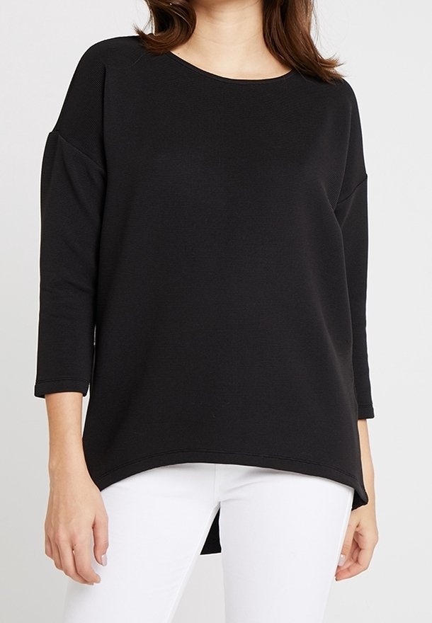 Musta pitkähihainen toppi, jossa on pyöreä pääntie, roikkuvat olkapäät ja kaareva helma. Kankaan pinnassa on hienovarainen teksturoitu kuvio.