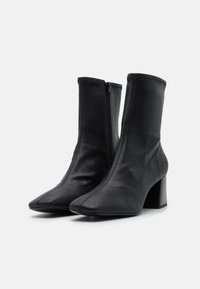 Botas de cuero negro hasta el tobillo con puntera afilada y tacón cuadrado. Cuentan con una cremallera lateral y una textura suave.