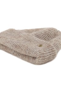 Złożona beżowa wełniana czapka z dzianiny o ryfrowanej strukturze i małym okrągłym metalowym emblematem na białym tle.