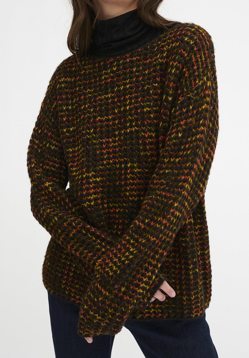Hřejivý svetr z hrubé příze v tmavě hnědé barvě s oranžovými, žlutými a zelenými cikcakovými vzory. Oversized střih s dlouhými rukávy a vysokým výstřihem.