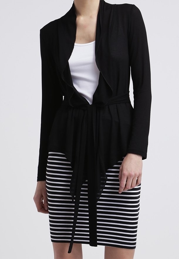 Černý zavinovací kardigán s volným designem a dlouhými rukávy, kombinovaný s upnutou pruhovanou sukní ke kolenům v černé a bílé barvě.
