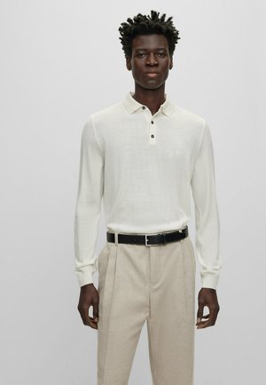 Långärmad ivory polo skjorta med stickad textur, tre svarta knappar vid kragen, ihopparad med ljusbeige skräddarsydda byxor och ett svart bälte.