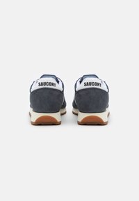 Navy blue suede sneakers with white accents, featuring a cushioned sole and raised branding on the heel. Textured lace-up front.