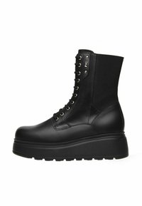 Stivale da combattimento in pelle nera con plateau, lacci frontali, suola spessa e pannello elastico nella parte superiore sul retro.