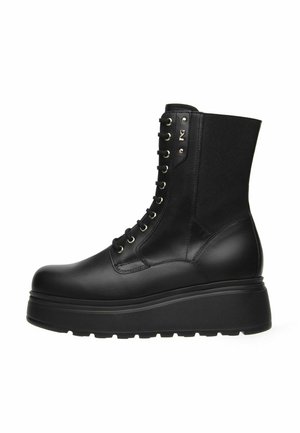 Stivale da combattimento in pelle nera con plateau, lacci frontali, suola spessa e pannello elastico nella parte superiore sul retro.