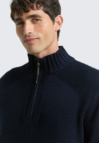 Marineblauer Pullover mit Reißverschluss, geripptem Kragen und strukturierten Schulterdetails, versehen mit einem goldfarbenen Reißverschluss und fleeceähnlichem Material.