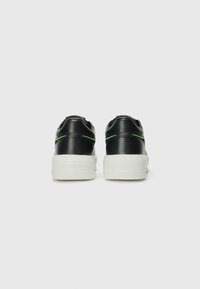 Zwarte leren sneakers met groene stikselaccenten, ronde neus, platte witte rubberen zool en reliëfbranding op de hak.